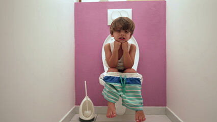 Obraz premium One cute small boy seated at toilet seat doing his needs at bathroom