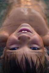 The boy smiles lying in the water. Large macro portrait. Cute kid relaxing in water and lying on...