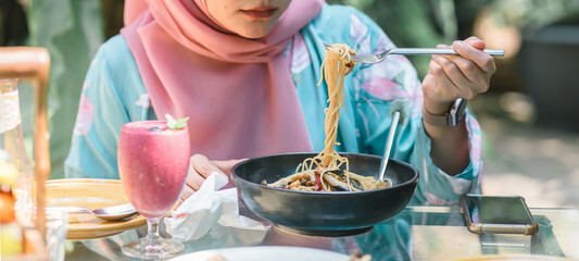 Cropped shot of happy young Muslim woman wearing a pink hijab, eating spaghetti outdoors during Ramadan celebration. Selective focus