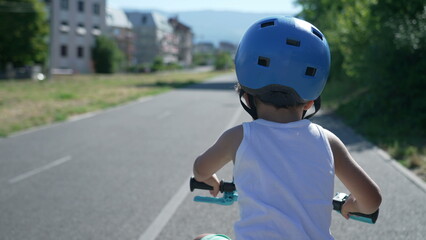 Fototapeta na wymiar Back of one active child wearing helmet riding bicycle outside in sunny day at bike lane in city