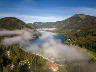 Aerial shot of a pond between forest mountains in a rural area on a foggy day in Mariazell, Austria