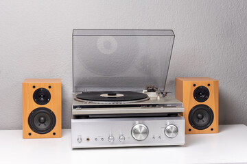 vintage vinyl player with amplifier and loudspeakers on white table