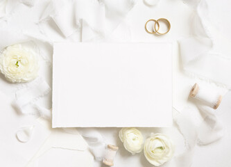 Obraz na płótnie Canvas Blank card near cream roses, white silk ribbons and wedding rings top view, wedding mockup