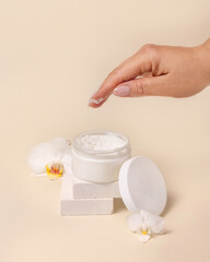 A woman hand using cream from Opened jar with a blank lid near orchid flowers, mockup
