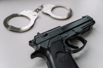 Arrest concept. Black handgun gun with handcuffs on wooden surface