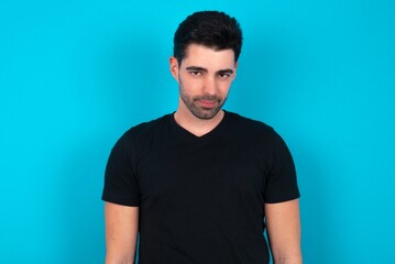 Fototapeta premium Young man wearing black T-shirt over blue studio background with nice beaming smile pleased expression. Positive emotions concept