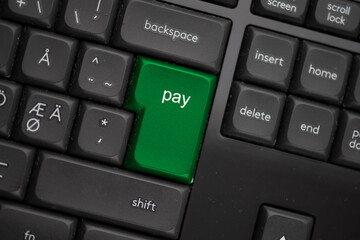 Computer keyboard with a green pay button.