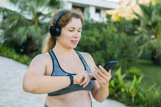 Young plus size woman with smart watch. Girl training in park. Woman with fitness tracker. Copy space and empty space for text - Powered by Adobe