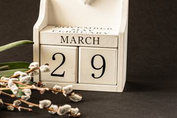 White block calendar presents month March, date 29th and willow branch, green leaves on dark background. Spring concept.  Background for product display