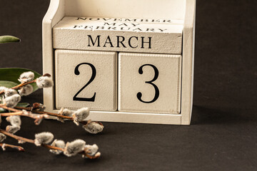 White block calendar presents month March, date 23th and willow branch, green leaves on dark...