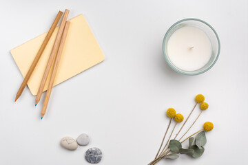 clean workspace with pencils and notebook, candle and flowers on white background. Flat lay