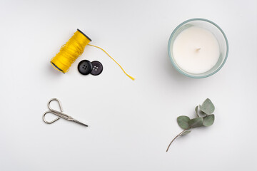 flat lay of scissors, yellow thread roll, buttons and candle on white background 