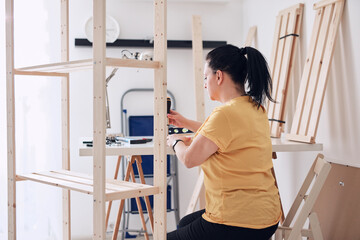 Obraz premium Woman assembling new wooden shelf and furniture in the apartment.