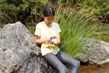 Asian girl having fun using a magnifying glass to look at Spirogyra in the stream. concept of...