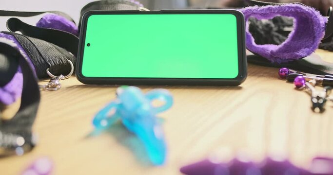 Rotating vibrator with rings around the edges on a background smartphone with green screen. Side view, close-up. Concept of an online app, store, sex shop.