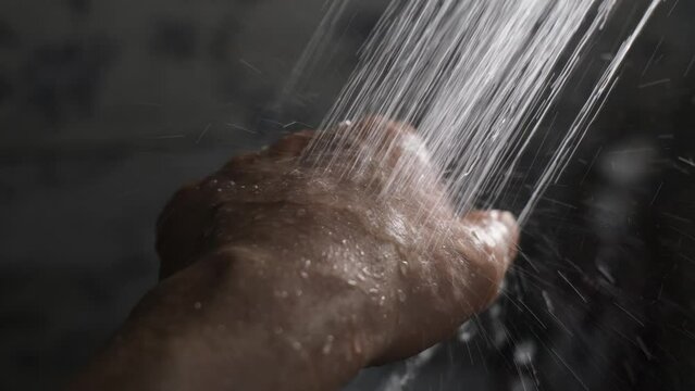 Water from the shower pours onto a man's hand in a stream, close-up