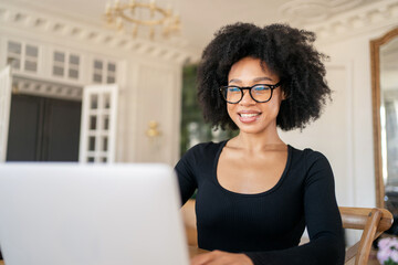 A curly-haired financier with glasses using an online computer. Wearing glasses, a young woman works in the office during the day.