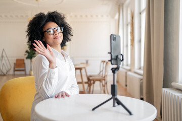 Freelancer curly-haired with glasses using a phone video call. Wearing glasses, a young woman works in the office during the day.