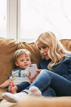 Mother And Child Sit On Couch Looking At Photos On Cell Phone