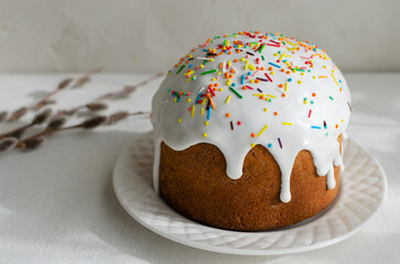 Traditional Ukrainian kulich on a white plate on a white tablecloth with willow buds. The concept of festive Easter baking. Selective focus. Horizontal orientation.