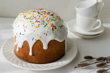 Traditional Ukrainian kulich on a white plate on a white tablecloth with willow buds. The concept of festive Easter baking. Selective focus. Horizontal orientation.