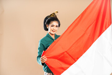 asian woman in green kebaya standing with smile while grabbing the indonesian flag on isolated background