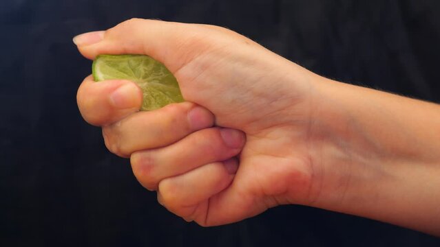 Hand squeezing lime on black background.