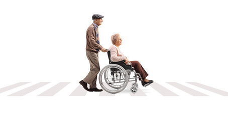 Full length profile shot of an elderly man pushing an elderly woman in a wheelchair at a pedestrian...