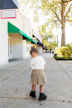 full length of baby girl in skirt and white t-shirt looking at acorns on ground in Miami.
