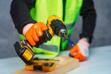 Male worker holds a close-up electric cordless screwdriver in his hands against the background of a construction tool and a concrete wall.