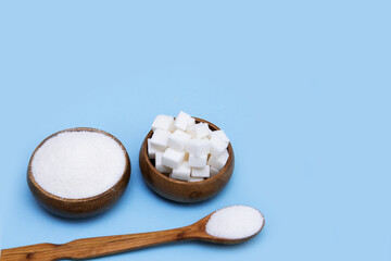 crystal white sugar, lump sugar in wooden bowls and wooden spoon on blue background with copy space