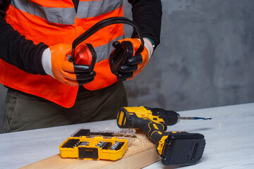 Male worker holds a close-up electric cordless screwdriver in his hands against the background of a construction tool and a concrete wall.