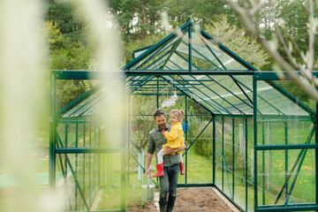 Father holding his little daughter in feco greenhouse,taking care of vegetable together, sustainable lifestyle.
