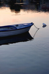 Small boat moored in shallow sea. Soft sunset light reflects in the sea. Selective focus.