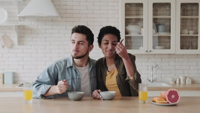 Happy multiethnic couple having breakfast in kitchen. Young African American woman and european man at home in the kitchen eating delicious healthy porridge with spoon