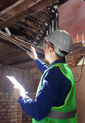 Building inspector. Man in a hard hat and a yellow reflective vest examines damaged structures and...