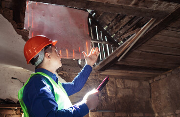 Building inspector. Man in a hard hat and a yellow reflective vest examines damaged structures and...