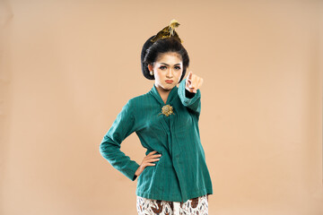 angry javanese woman in green kebaya standing with sullen face while put her hand on her waist and pointing forward on isolated background
