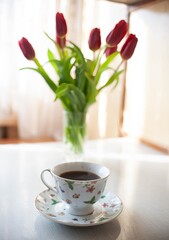 Fototapeta na wymiar Cup of coffee next to bouquet of flowers