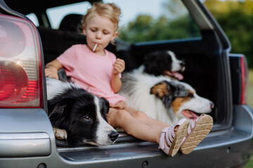 Little girl and her dogs sitting in a car, prepared for family trip,