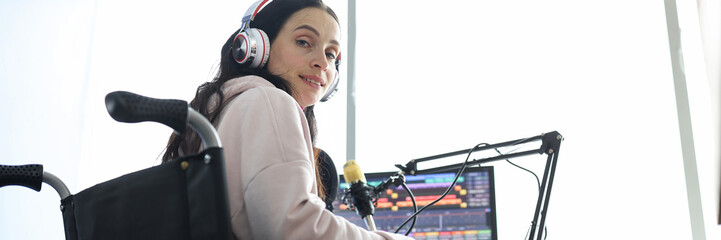 Female freelancer programmer or streamer in modern headphones sits in wheelchair and uses computer