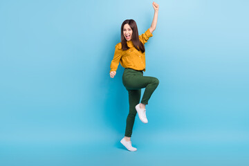Fototapeta na wymiar Full length photo of cool lucky woman wear yellow shirt smiling rising fists isolated blue color background