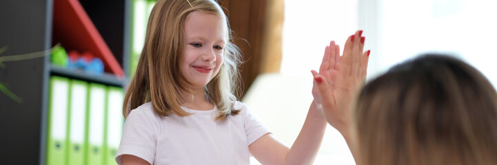 Happy little preschool girl giving high five to doctor at meeting in hospital