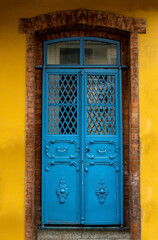 Old blue metal door with brick frame in yellow wall.