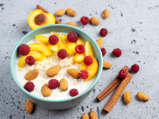 Healthy breakfast, milk oatmeal with raspberries, peach and almonds