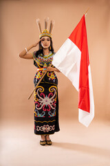 beautiful woman in king bibinge standing with salutation and holding the indonesian flag on...
