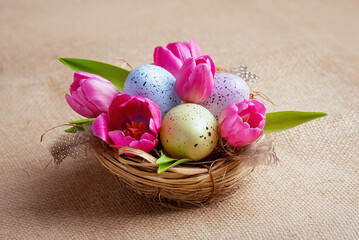Obraz na płótnie Canvas Happy easter! Nest with multi-colored eggs and pink tulips on a canvas background.