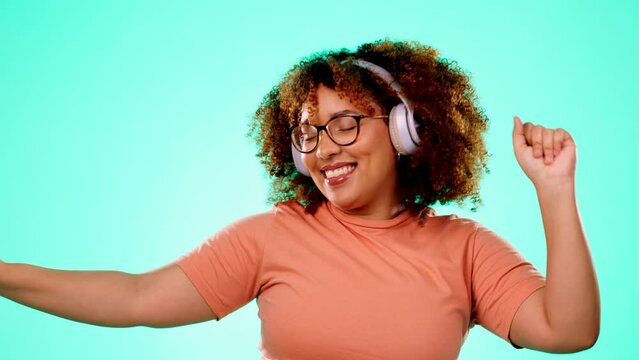 Headphones, music and dancing black woman in studio with happy turquoise background and smile with happiness. Fun, streaming service and dance, excited African person with online radio station app.