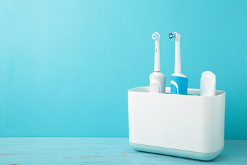 Holder with modern electric toothbrushes on blue background