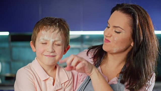 Happy mother kisses her son in the kitchen. The family prepares dough with flour together. Lifestyle children fool around with their parents and have fun at home. High quality 4k footage